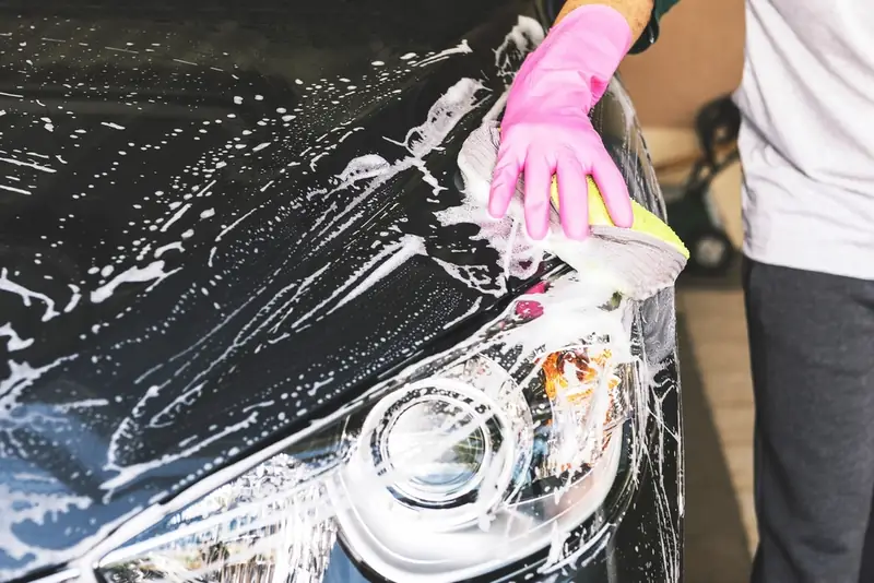 A gloved hand washing a soapy black bonnet